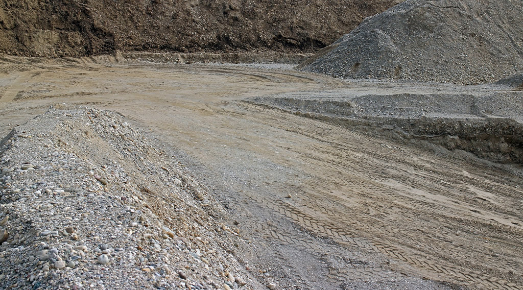 Големи количества сив и кафяв пясък със следи от гуми на камиони